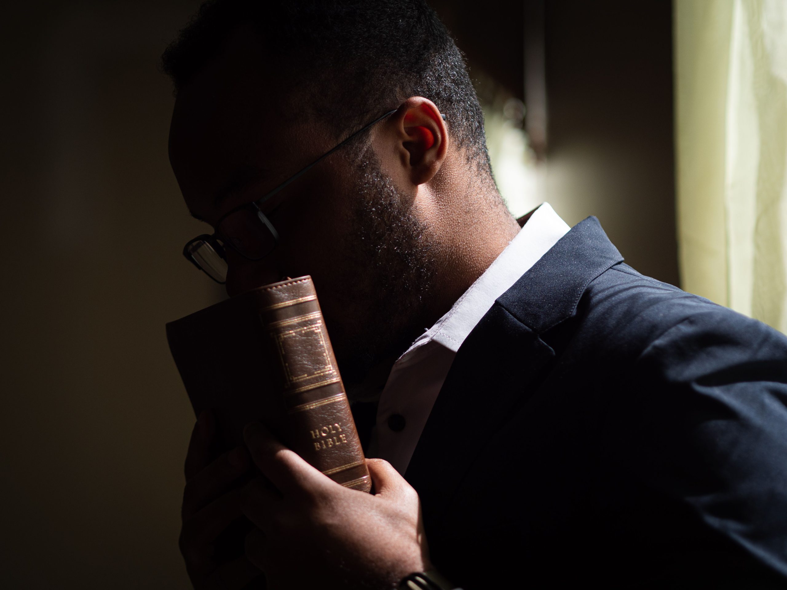 Home A man in a blue suit holds a Bible close, symbolizing contemplation and faith.