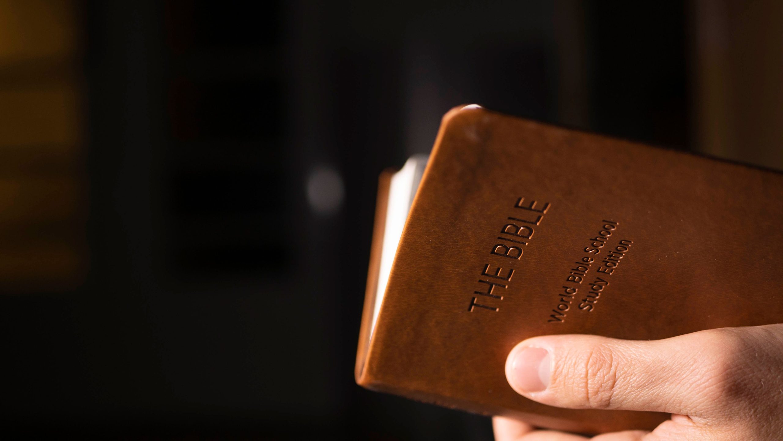 Home Detailed view of a hand holding a leather-bound Bible indoors.